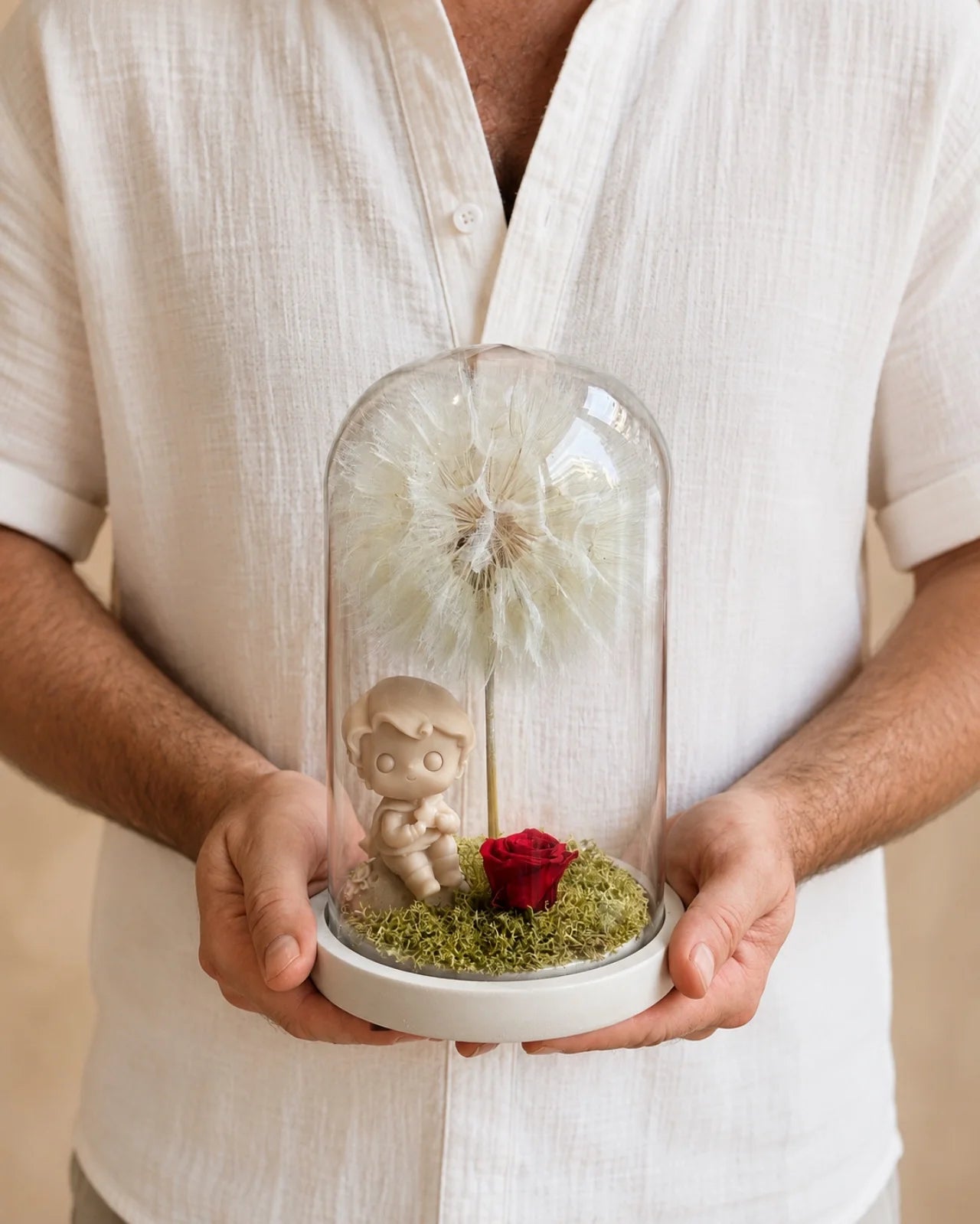 Mani che tengono la campana di vetro L'Essentiel — composizione botanica ispirata a Le Petit Prince, Io Sono La Luce Roma.