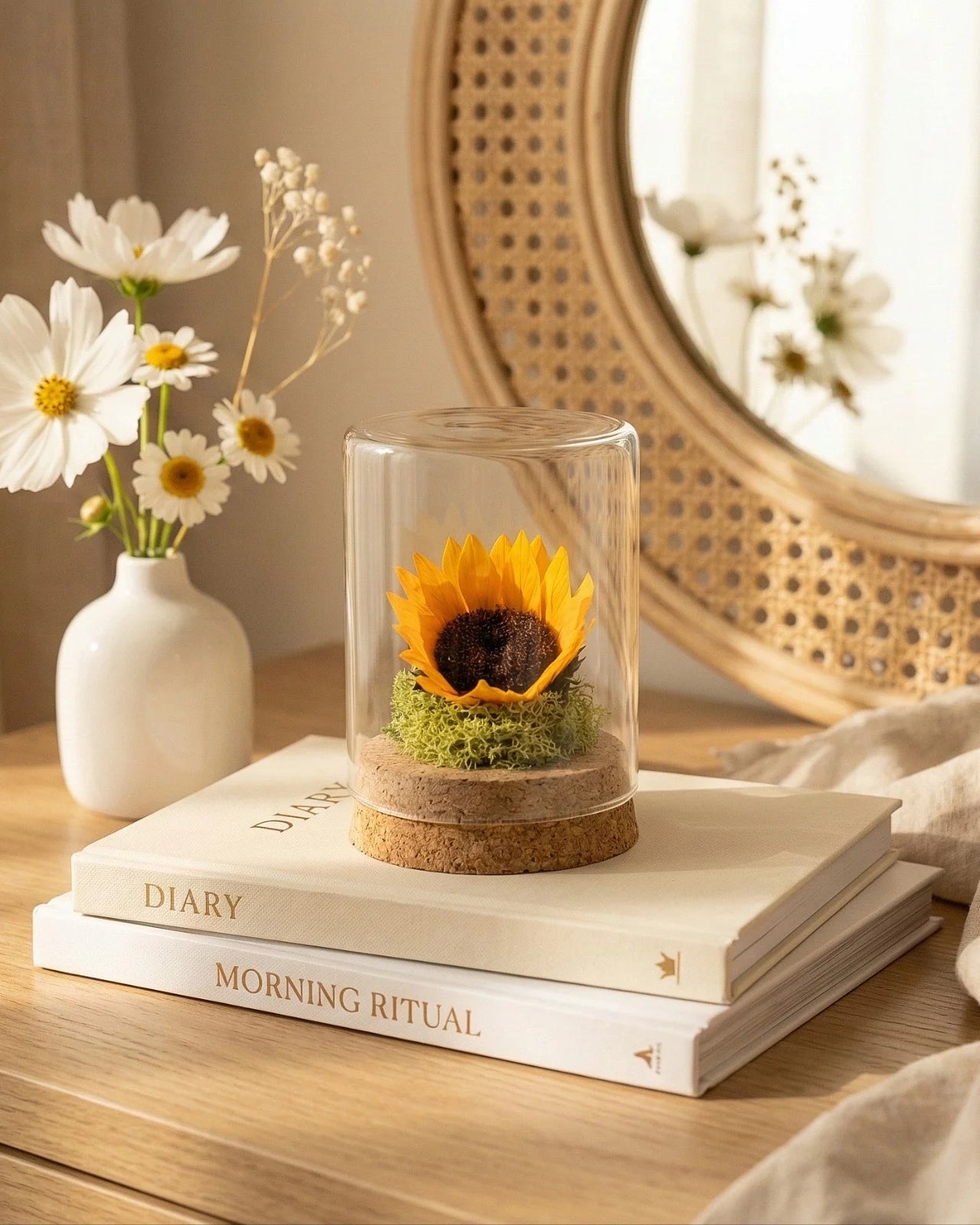Girasole eterno sotto vetro su console con libri e specchio rattan, decorazione vanity naturale elegante