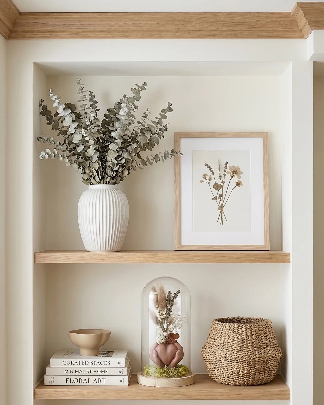 Composizione botanica artigianale con fiori secchi e stabilizzati sotto campana di vetro su base in legno naturale
