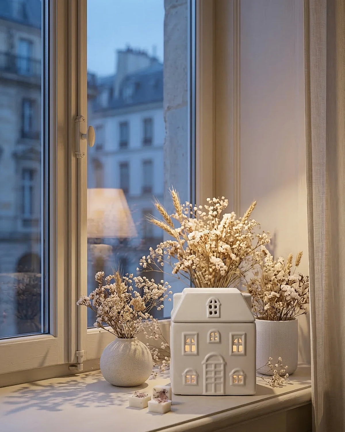 Bruciatore di cera in ceramica bianca a forma di casetta Akari No Ie, vista frontale con finestrelle ritagliate e luce soffusa che filtra dalle finestre
